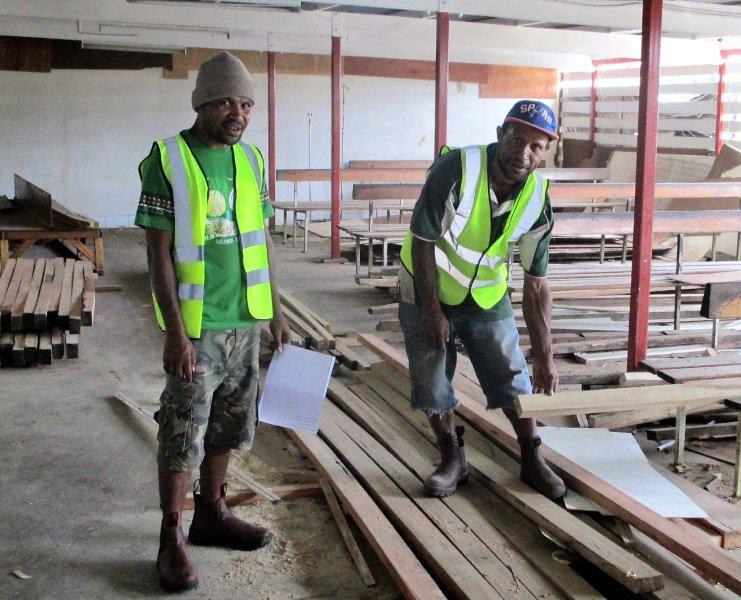 Project Supervisor, Stanis Pilakue (left) watches as a carpenter sorts out some timber to be used.