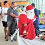 Santa Claus accompanied by her helpers meets a child and her mother.