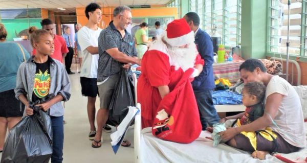 Santa Claus accompanied by her helpers meets a child and her mother.