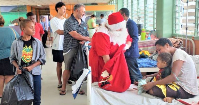 Santa Claus accompanied by her helpers meets a child and her mother.
