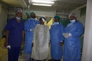 Marian Kerai, glowing in her white gown, poses with Dr. Wahamu and the dedicated eye surgical team following a successful cataract procedure